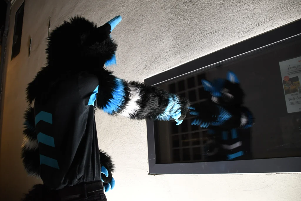 Photo of a fursuiter seeing themself in a darkened screen