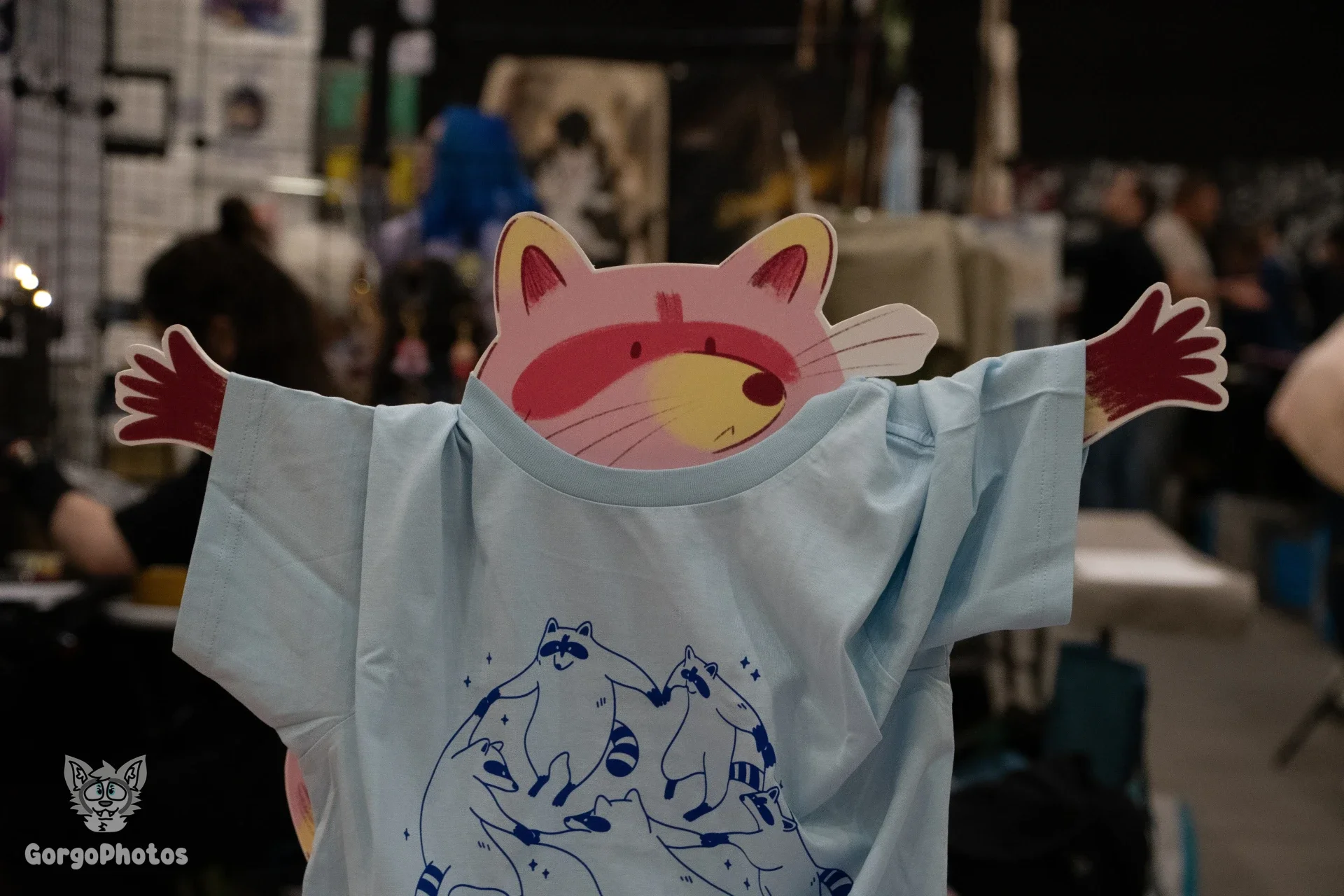 A cardboard cartoon raccoon wearing a t-shirt that shows cartoon raccoons dancing.